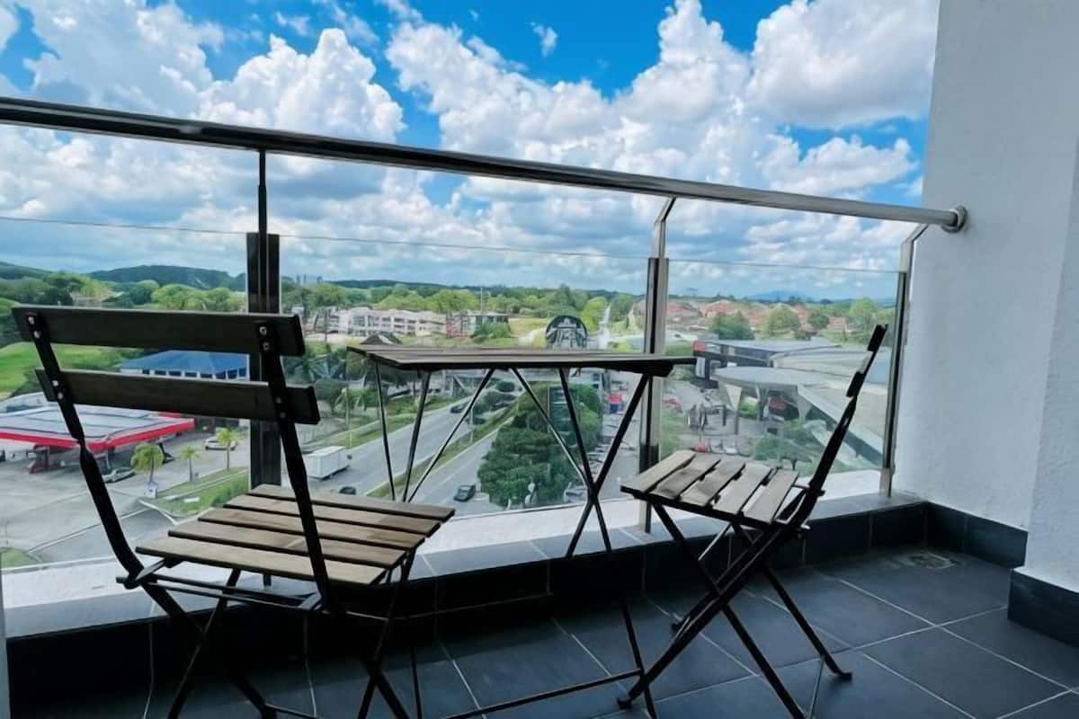 A balcony with two wooden chairs and a table, overlooking a cityscape with buildings and a road.
