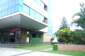 A modern building with a glass facade, a covered entrance, and a statue in the garden.