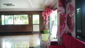 A spacious lobby with a large window, a pink artificial tree, and a red sofa. - SVR Hotel Sai Samrat (Rahata)