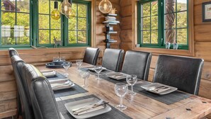Ein Esszimmer einer Holzhütte mit einem großen Tisch, gedeckt für sechs Personen, Ledersesseln und hängenden Lampen.
