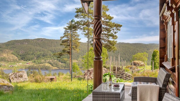 Eine Holzterrasse mit Korbmöbeln, mit Blick auf einen See und bewaldete Hügel.