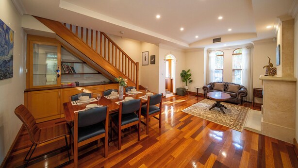 A spacious living room with a wooden staircase, a dining area with a wooden table and chairs, a fireplace, and a cozy seating area with a sofa. - Cozy Home with fireplace 5mins to beach (Glenelg)