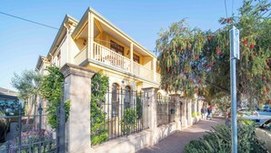 A two-story building with a balcony, a wrought iron fence, and a paved walkway. - Cozy Home with fireplace 5mins to beach (Glenelg)