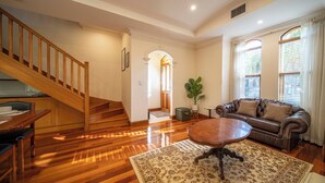 A spacious living room with a wooden staircase, a brown leather sofa, a round coffee table, and a patterned rug. - Cozy Home with fireplace 5mins to beach (Glenelg)