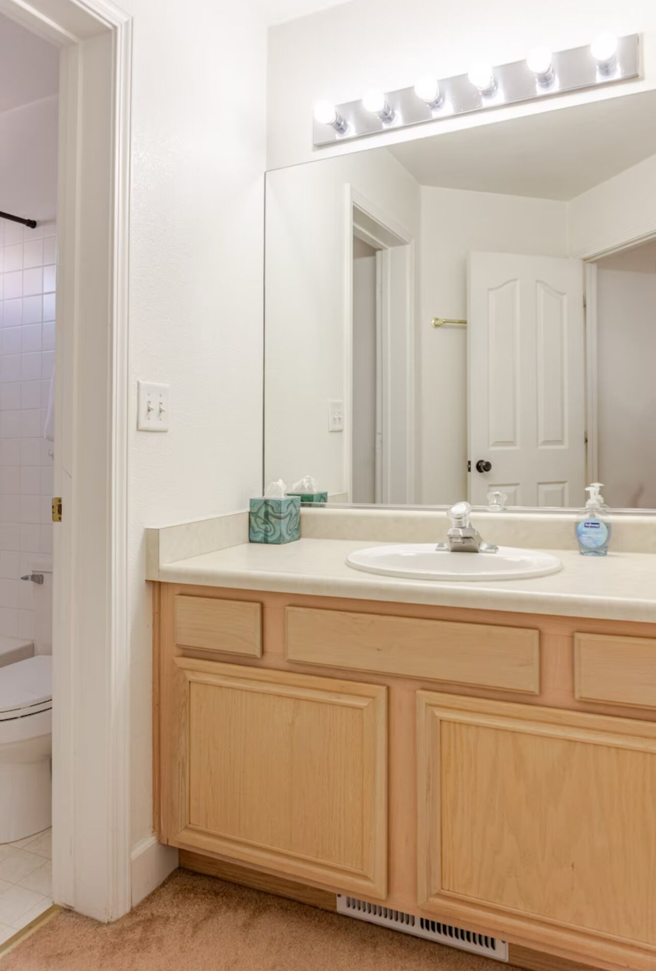 Un baño con tocador blanco, un espejo grande con luces y un lavabo.