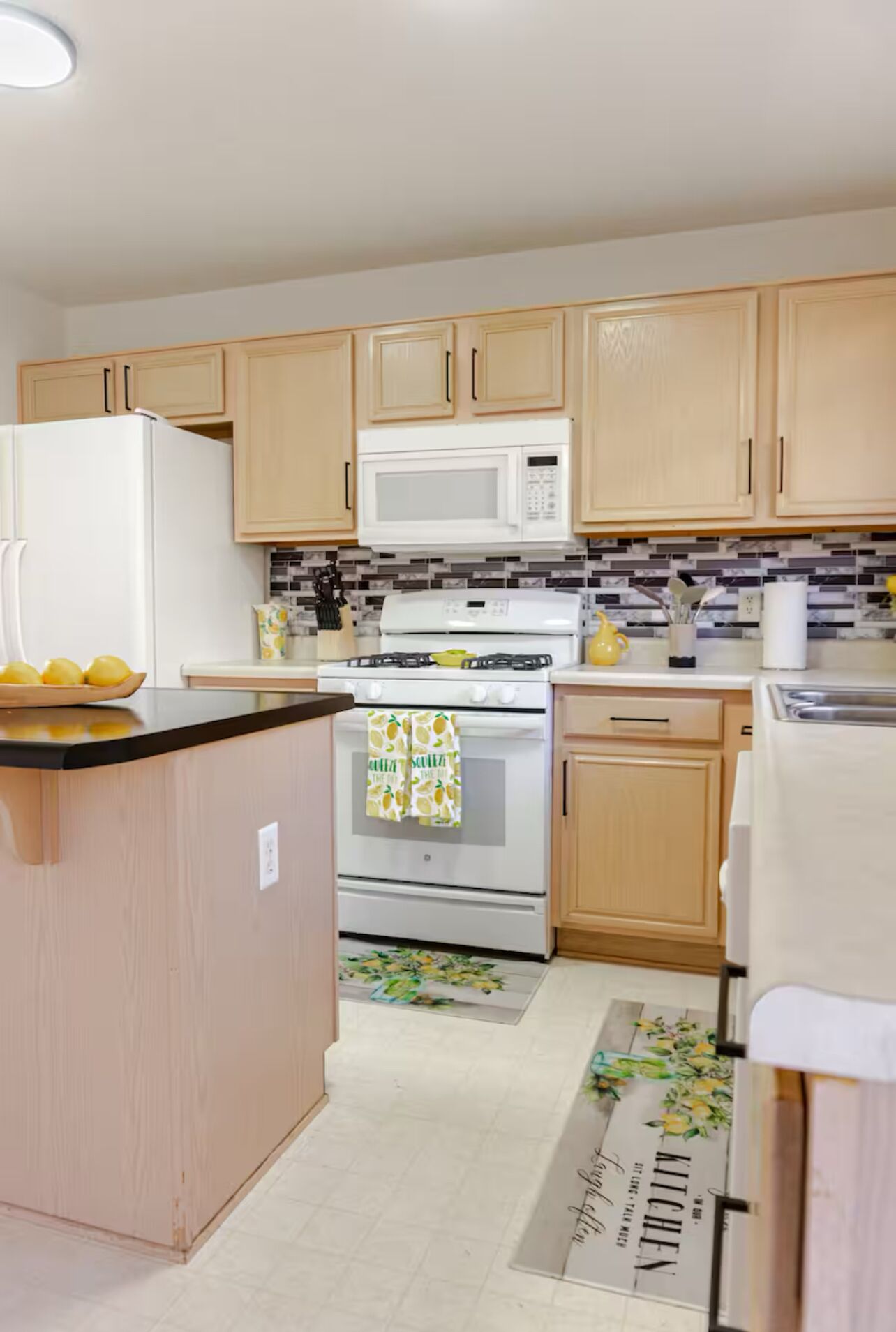 A kitchen with wooden cabinets, a white refrigerator, a microwave, an oven, and a sink.