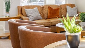 Un salon avec un canapé en cuir marron, deux fauteuils, une table basse en verre et une plante en pot.