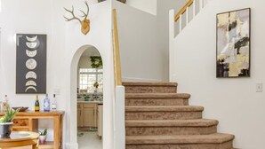 Un escalier avec une rampe en bois menant à un palier. Au-dessus de l’escalier, un décor mural représentant une tête de cerf est fixé au mur.