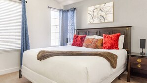 Une chambre à coucher avec un grand lit, une table de chevet, une fenêtre avec des stores et un tableau au mur.