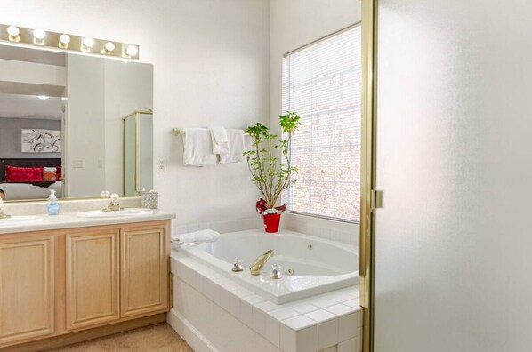A modern bathroom with a large bathtub, a vanity with a mirror, and a potted plant.