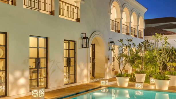 A swimming pool area with a white building, arched windows, and potted plants.