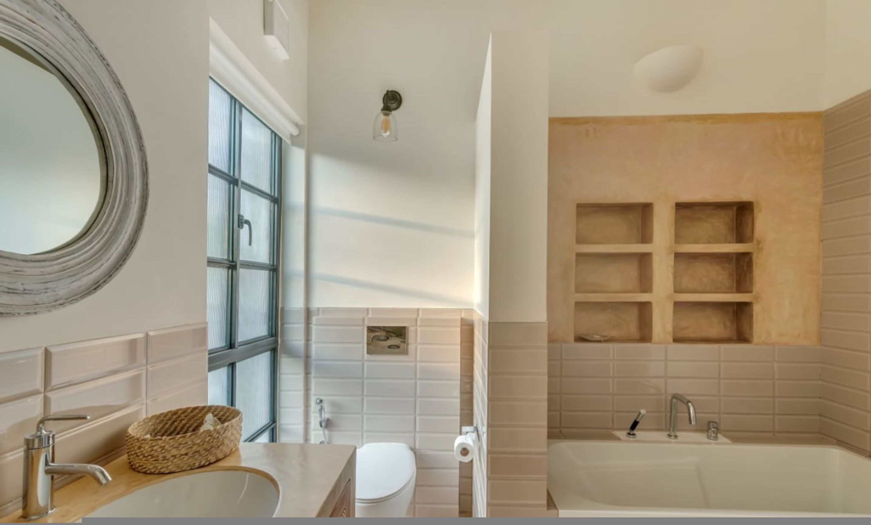 A bathroom with a large mirror, a window, a toilet, and a bathtub with shelves.