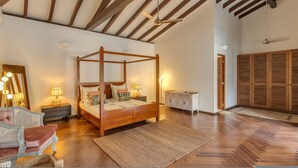 A spacious bedroom with a four-poster bed, wooden flooring, and a ceiling fan.