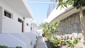 A narrow pathway flanked by white buildings with a stone wall on one side and a row of tropical plants on the other. - 711 Cumana2 Puerto Rico By Alquiler de Sueño (Puerto Rico de Gran Canaria)