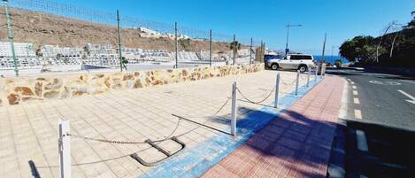 A paved area with a chain barrier, a white vehicle, and a road with a blue line.