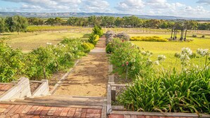 Ein Weg führt durch einen Garten mit einer Pergola und Blick auf einen Weinberg in der Ferne.