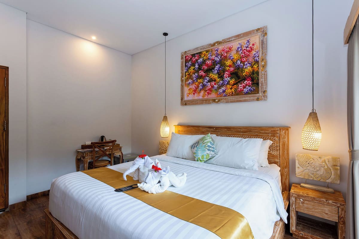 A hotel room with a large bed, a wooden headboard, a painting of flowers on the wall, and two bedside lamps.