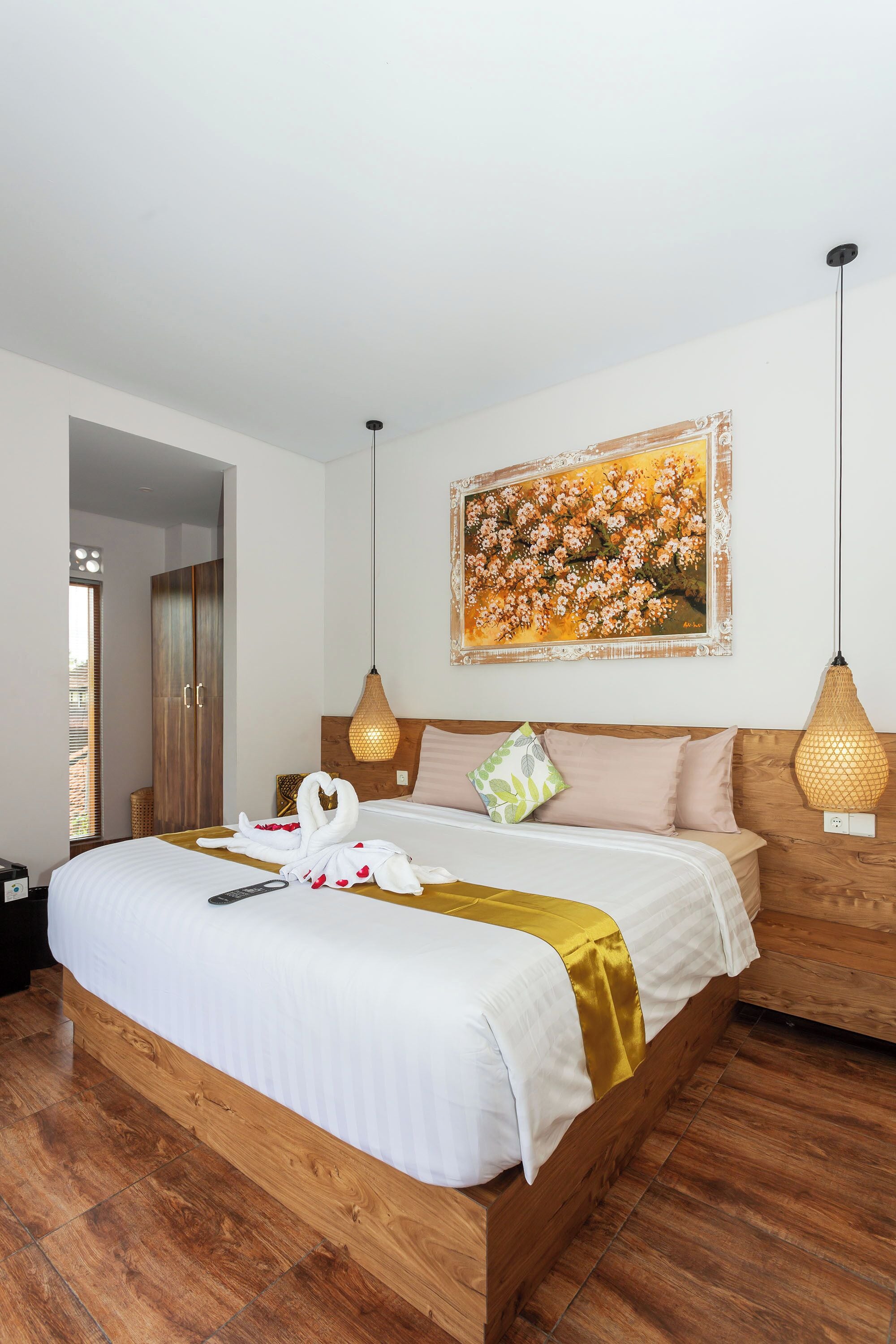 A hotel room with a wooden bed, a painting on the wall, and two pendant lights.