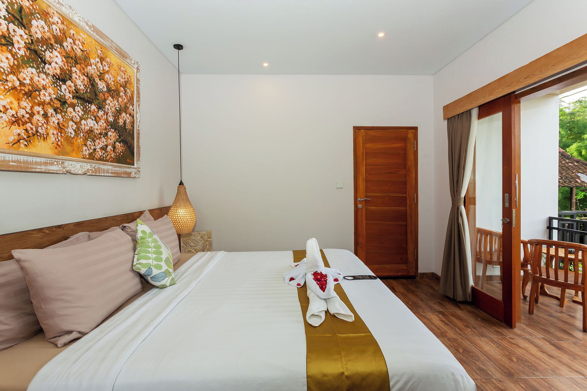 Quarto de hotel com uma cama, um quadro, uma luminária pendente e uma porta que dá para uma área externa.