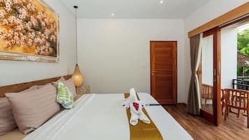 Quarto de hotel com uma cama, um quadro, uma luminária pendente e uma porta que dá para uma área externa.