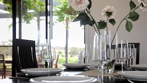 Una mesa de comedor lista para una comida, con platos blancos, cristalería transparente y un florero con flores.