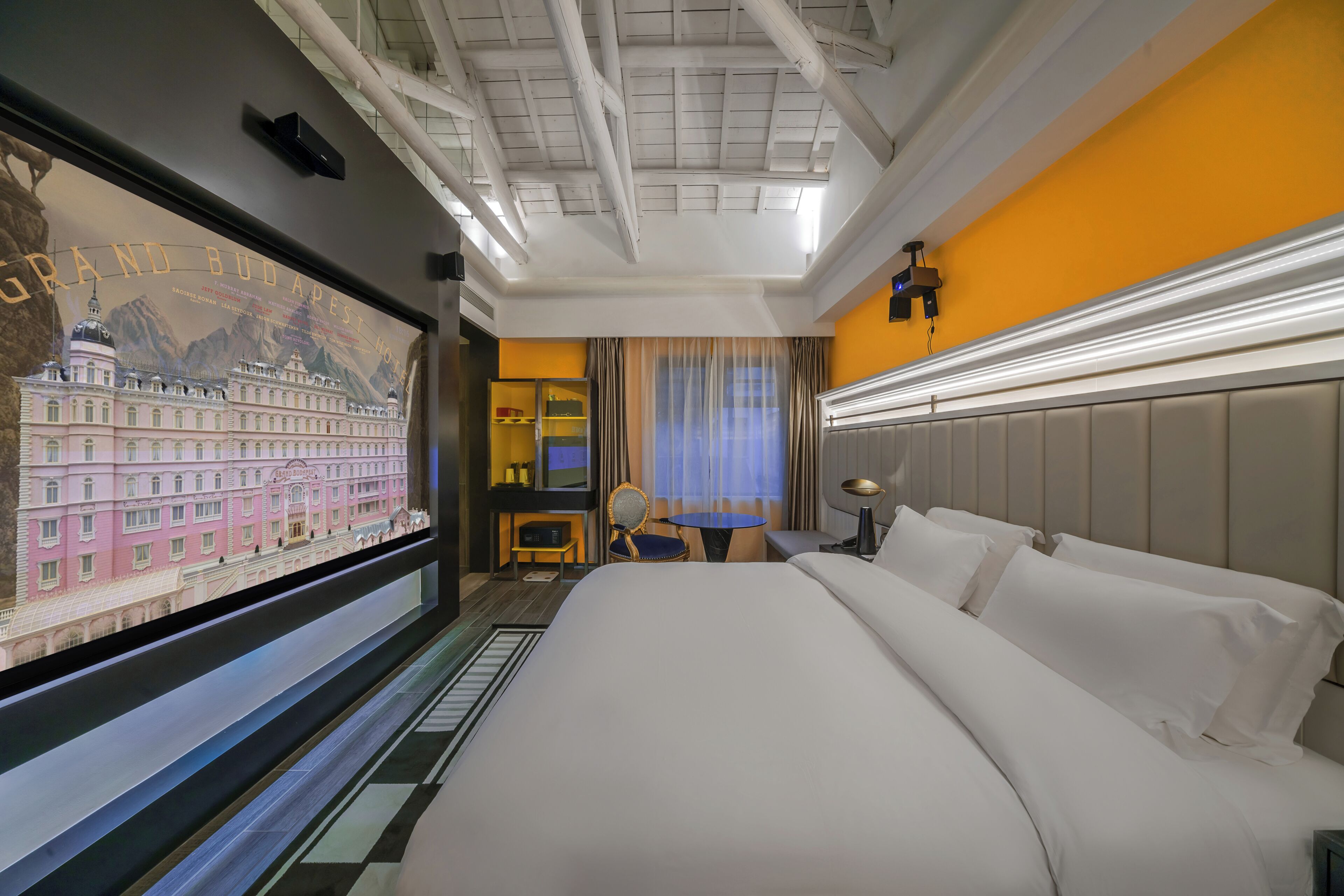 Una habitación de hotel con una cama grande, un escritorio, una silla y un televisor que muestra una vista urbana.