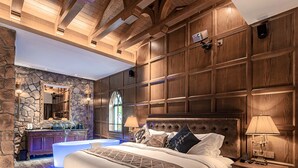 Ein geräumiges Schlafzimmer mit einem großen Bett, Holzbalken an der Decke, Steinwänden und einem Kamin aus Stein.