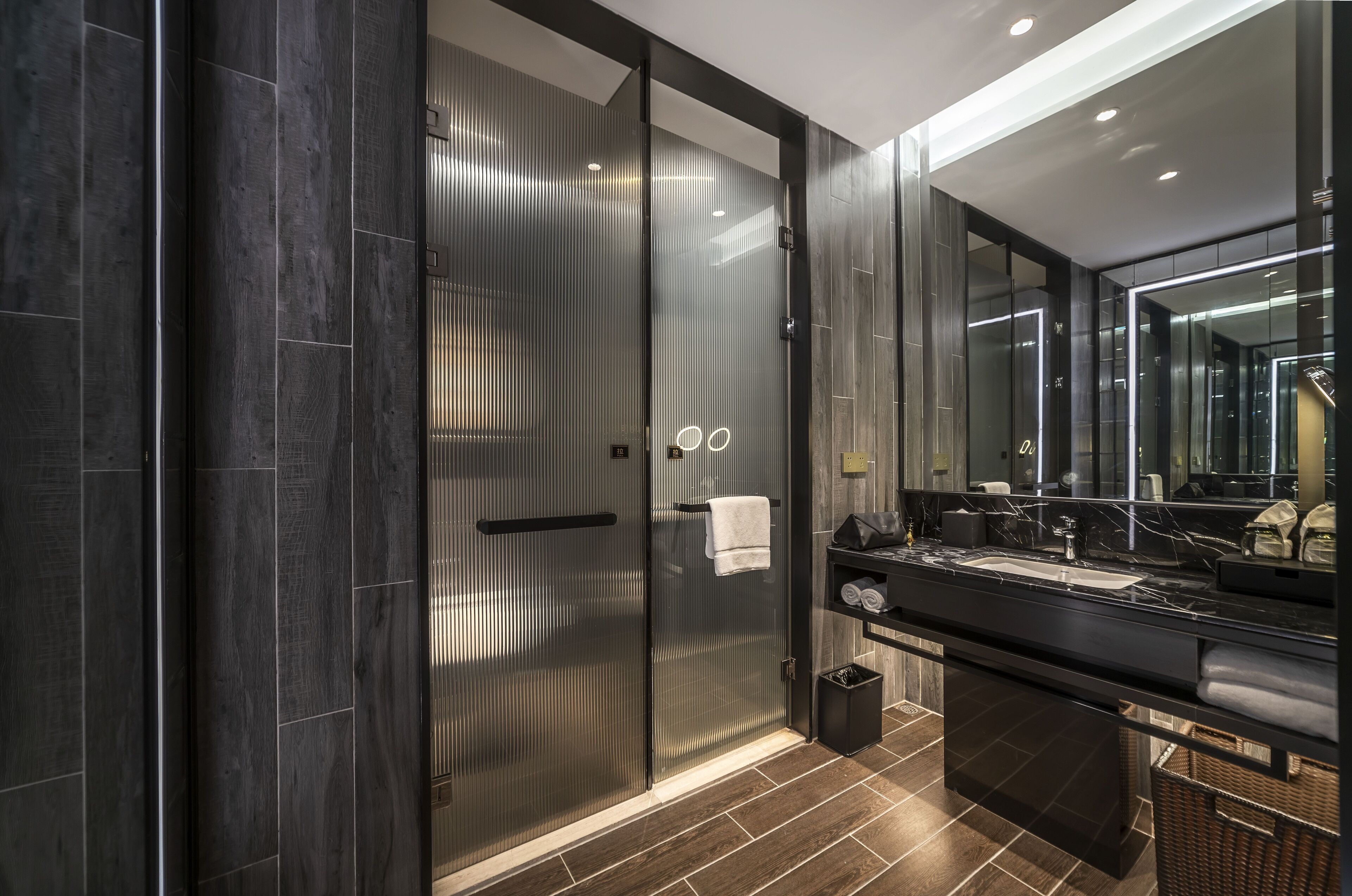 A modern bathroom with a glass shower enclosure, a large mirror, and a dark-toned vanity.