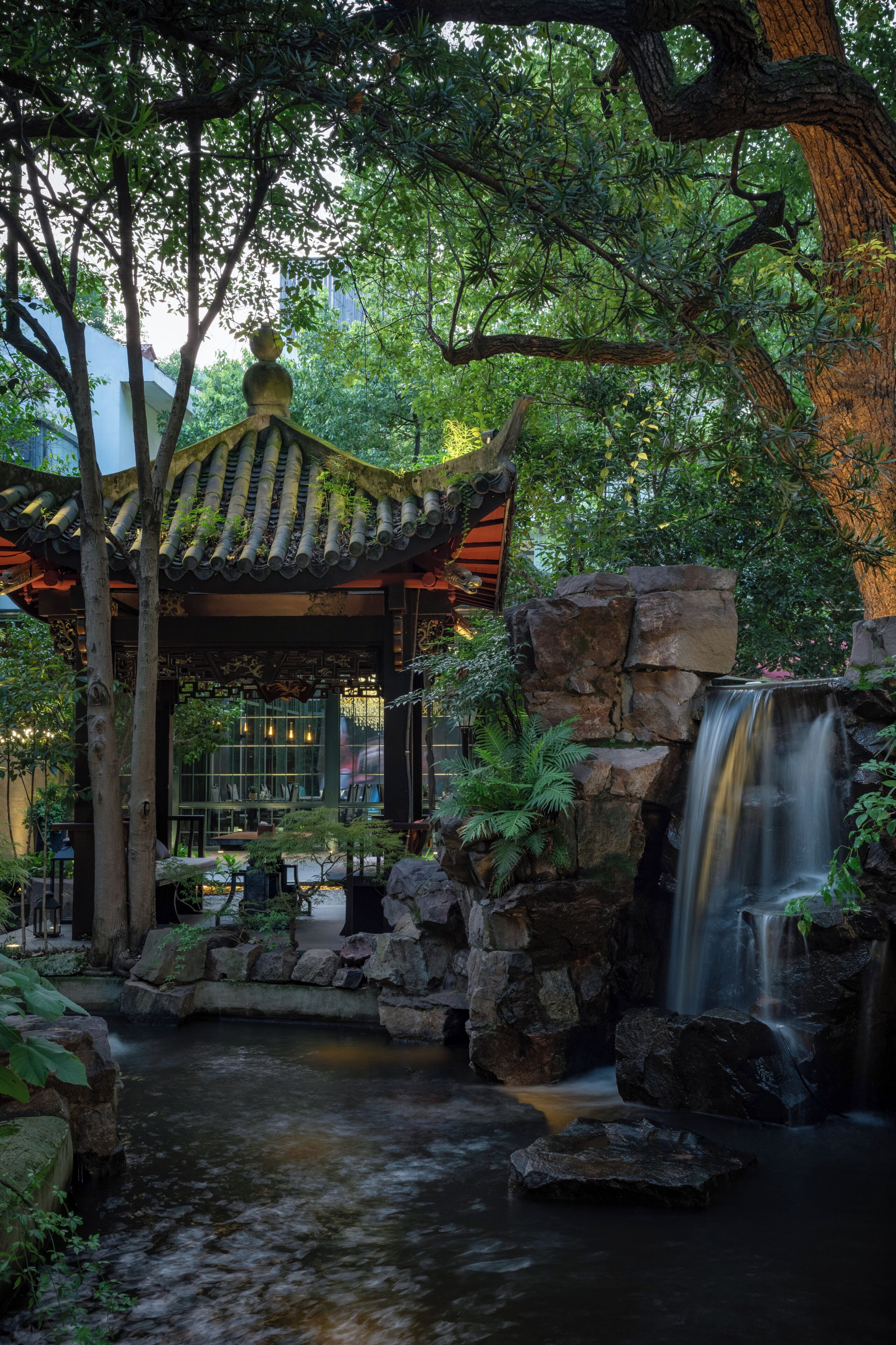 A traditional pavilion with a stone waterfall and a small pond.