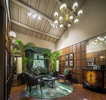 Amplia habitación con techo alto, candelabro, sofás de cuero, una mesa de centro y un mueble de madera con cuadros enmarcados.