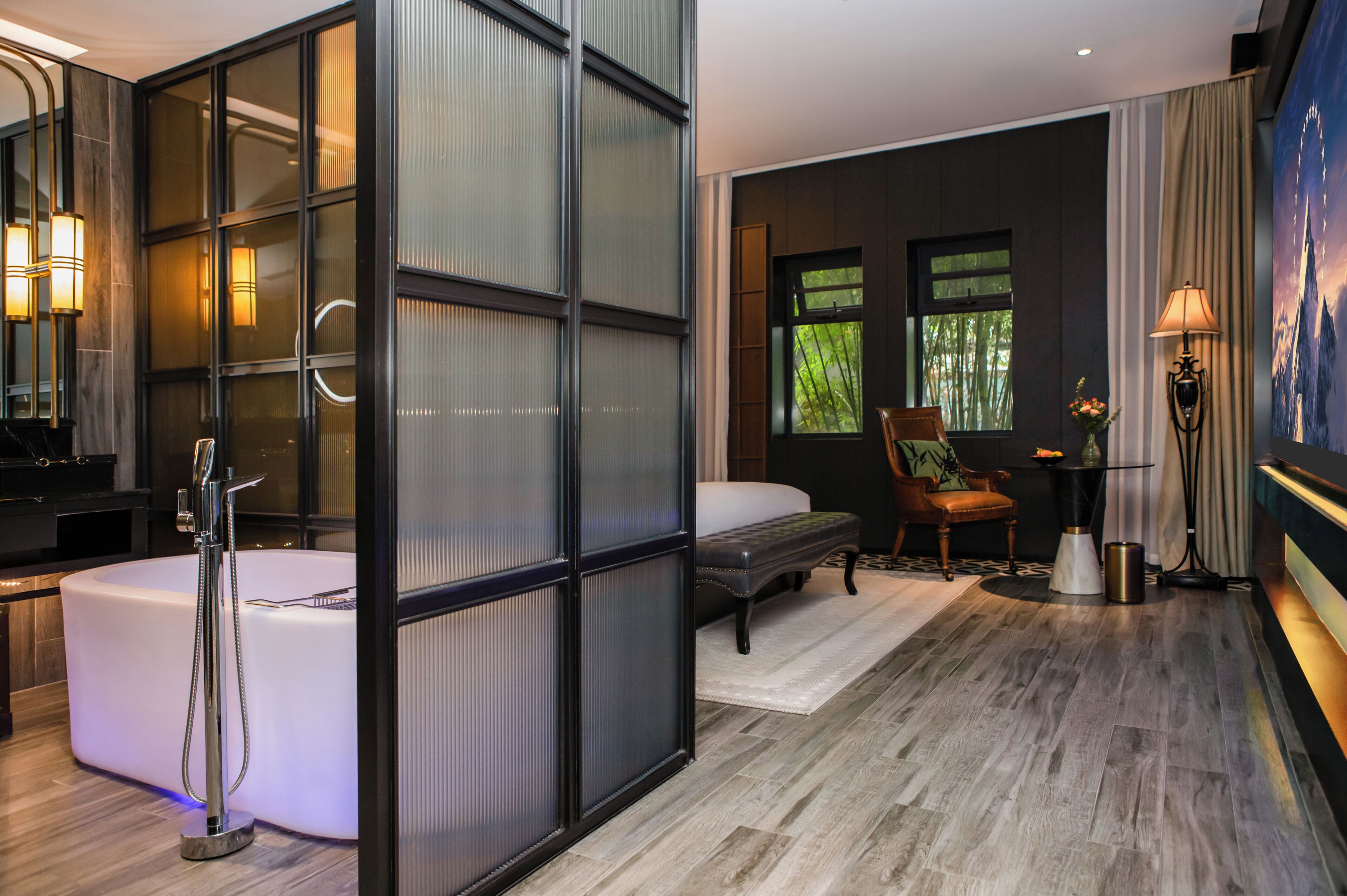 Un baño moderno con bañera, ducha y mampara de cristal. Hay una cama, una silla y una mesa con una lámpara.