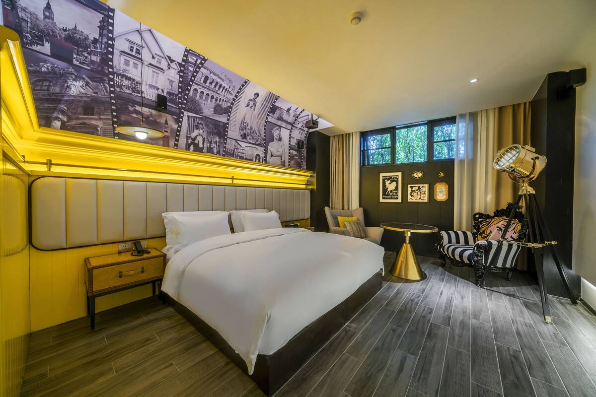 Een hotelkamer met een groot bed, een nachtkastje, een klein tafeltje, een stoel en een decoratieve lamp.