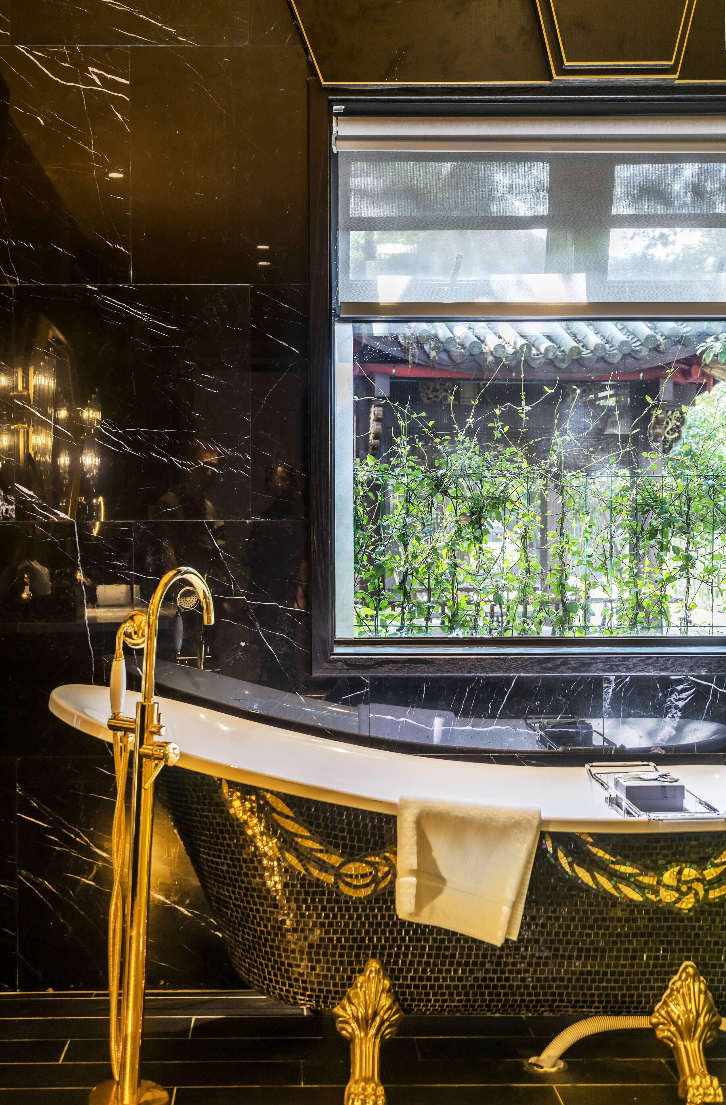 Un baño con bañera, grifo dorado y ventana con vista a follaje.