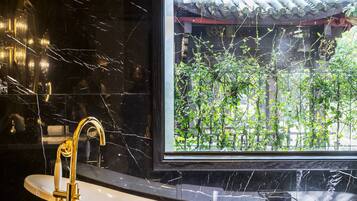 Un baño con bañera, grifo dorado y ventana con vista a follaje.