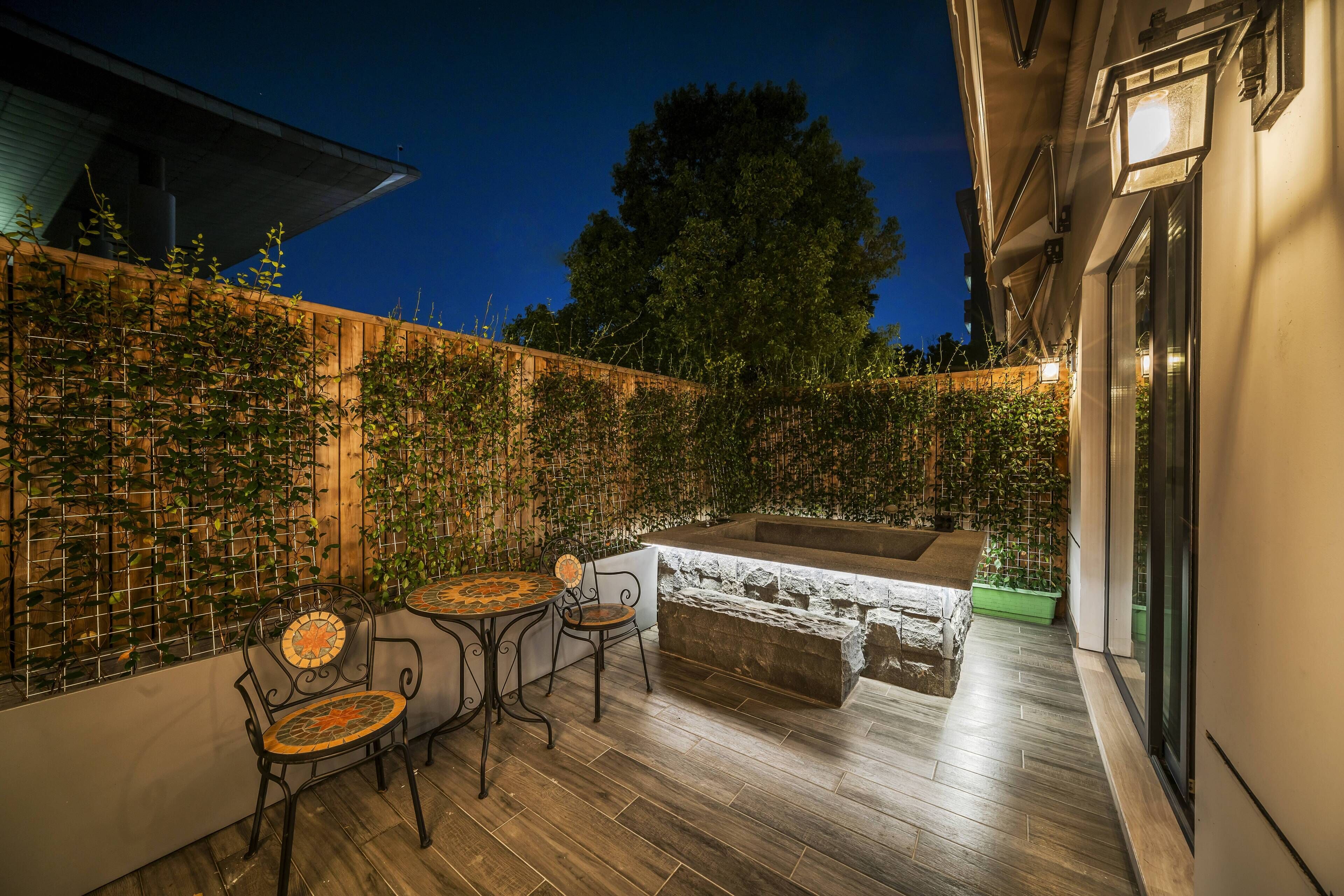 An outdoor patio with wooden flooring, two metal chairs, a small table, and a stone bench.