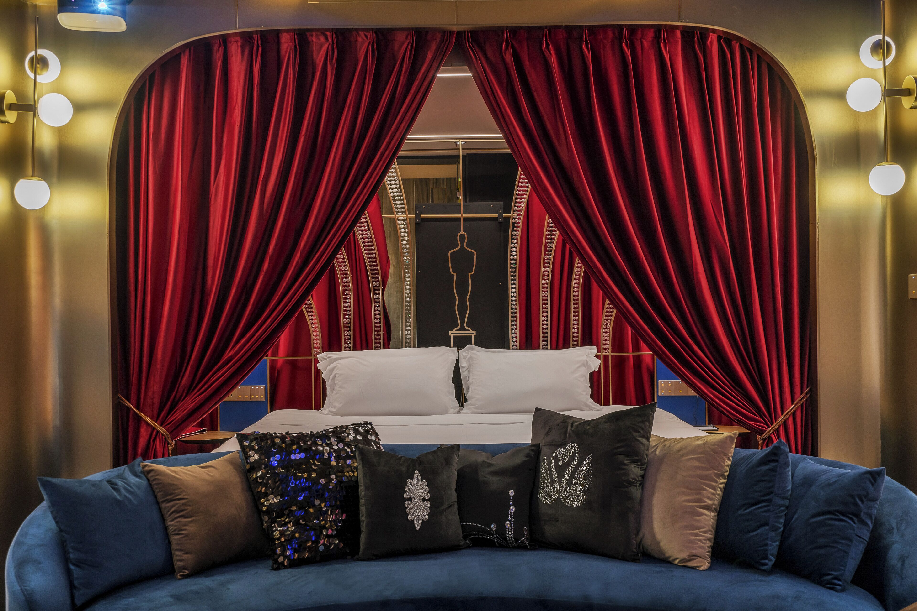 A bedroom with a large bed, red curtains, a mirror, and a blue sofa with decorative pillows.