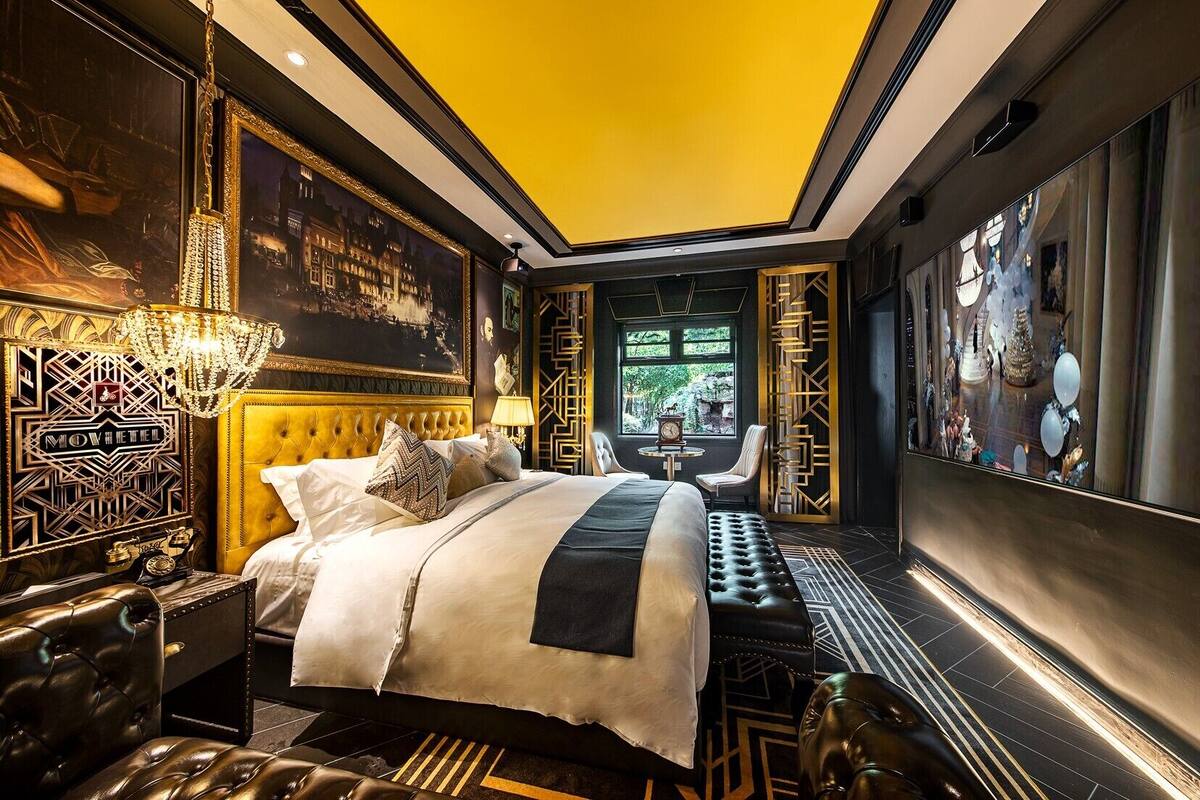 Een luxueuze slaapkamer met een gestoffeerd hoofdeinde, een groot bed met witte lakens, een kroonluchter en uitzicht op een besneeerd landschap door een raam.