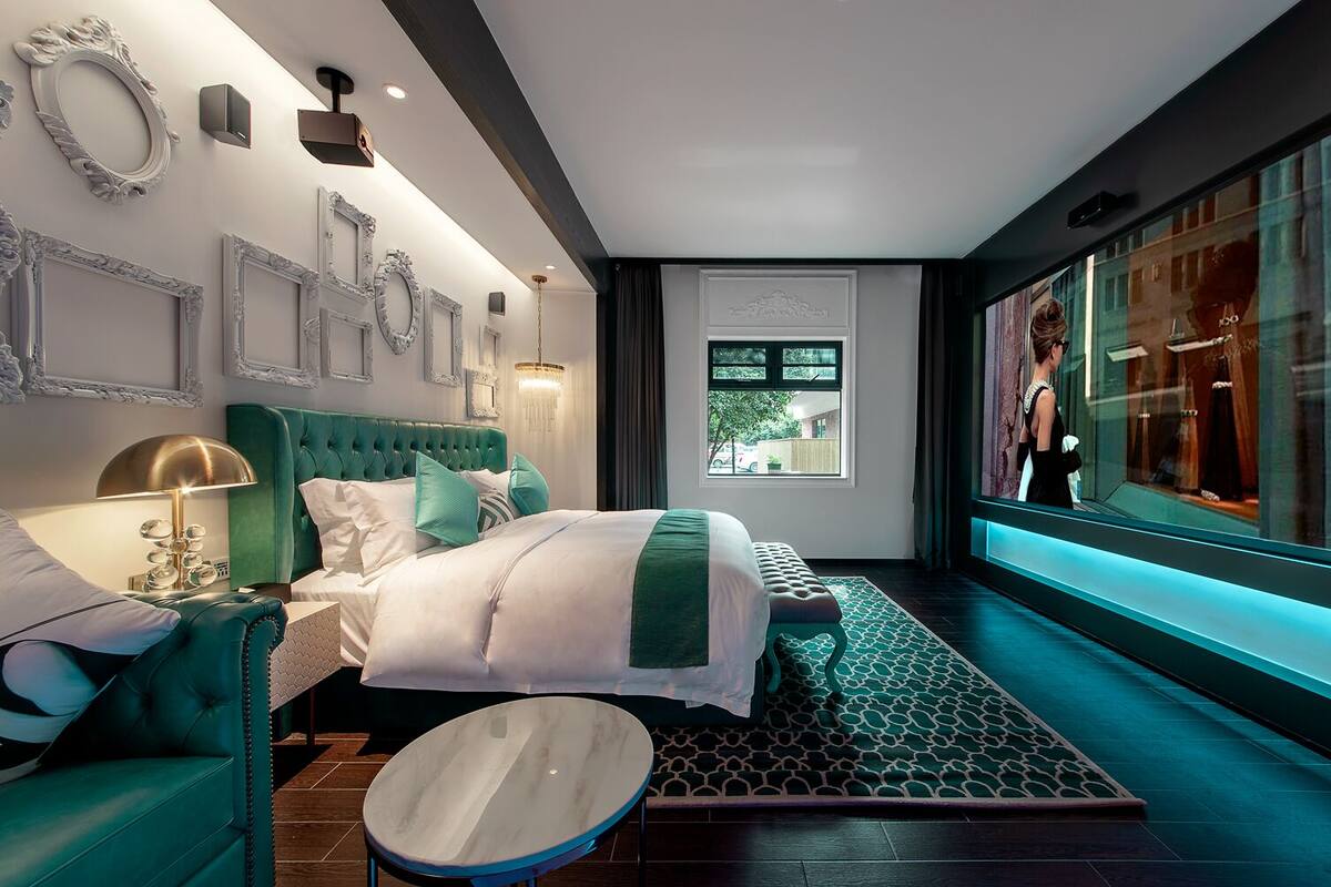 Een moderne slaapkamer met een groen bekleden hoofdeinde, een rond nachtkastje van marmer en een groot raam met uitzicht.