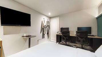 Une chambre d’hôtel avec un lit, un bureau équipé de deux ordinateurs, une télévision et une petite table sur laquelle se trouve une boîte de mouchoirs.