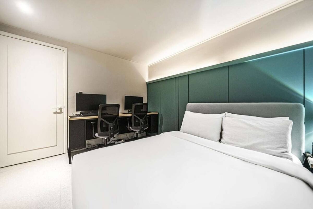 A hotel room with a bed, two desks with computers, and a green accent wall.