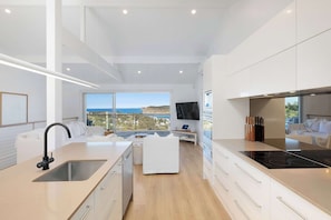 A modern kitchen with a large island, a built-in oven, and a view of the sea.