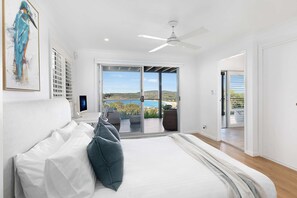 A bedroom with a bed, a ceiling fan, a large window with a view, and a door leading to a balcony.