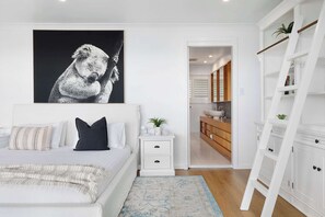 Une chambre à coucher avec un lit, des tables de chevet, une commode, un tableau accroché au mur, une armoire blanche et un plancher en bois.