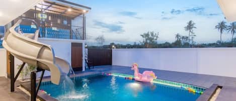 A swimming pool with a slide, a pink flamingo float, and a view of palm trees.