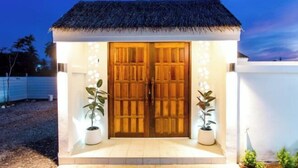 A small, single-story building with a thatched roof, two wooden doors, and potted plants on either side.