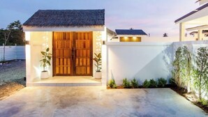 A modern house with a thatched roof entrance, a concrete patio, and potted plants.