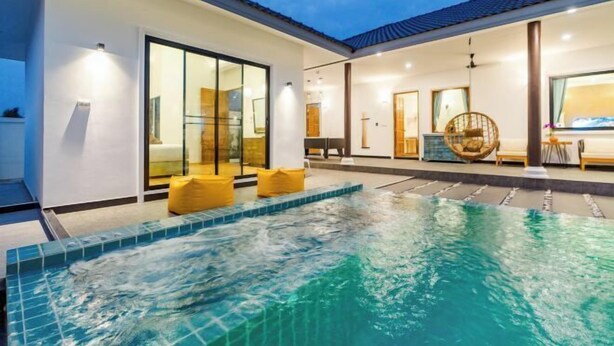 A modern outdoor swimming pool with a glass-enclosed patio area, a ceiling fan, and a seating area with cushions.