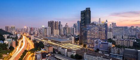 A cityscape with a prominent modern building featuring a unique curved design, surrounded by other high-rise buildings and a well-lit train station.
