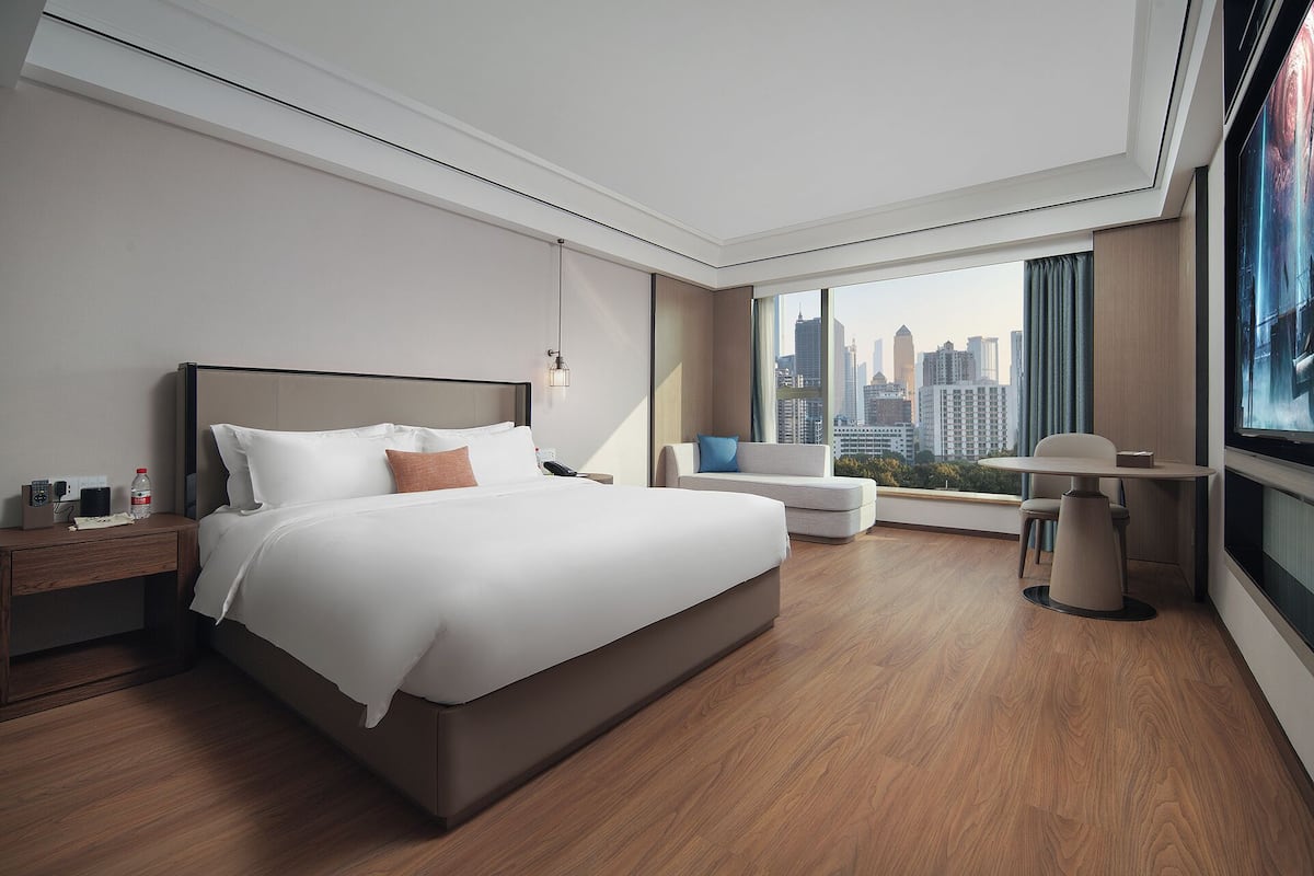 Une chambre d’hôtel moderne dotée d’un grand lit, d’un canapé, d’un bureau et offrant une vue sur le panorama urbain.