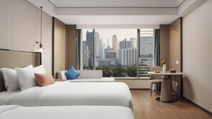 A modern hotel room with two beds, a small table, and a city view.